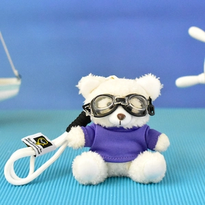 Detailed view of a white plush teddy bear charm wearing purple shirt and goggles