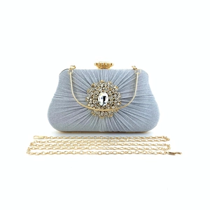 Detailed view of silver pleated clutch bag featuring crystal buckle and gold chain strap