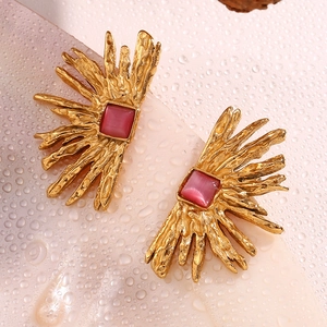 Macro shot of gold-plated starfish shell earrings with pink stones on wet surface