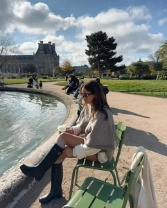 Elegant camel knit poncho paired with black boots in a stylish Parisian outdoor setting