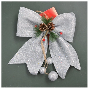 Detail of silver glitter Christmas bow with pine cone and red berries on green background