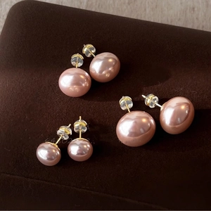 Three pairs of pink pearl stud earrings in different sizes on a brown velvet stand