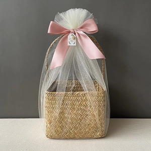 Detail of seagrass basket with white mesh wrap and a large pink ribbon bow for gifts