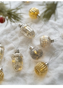 Detail of glass pine cone and pumpkin string lights on snow with warm glowing effect