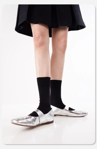 Nahaufnahme silberner Mary Jane Halbschuhe mit schwarzen Socken und einem Faltenrock