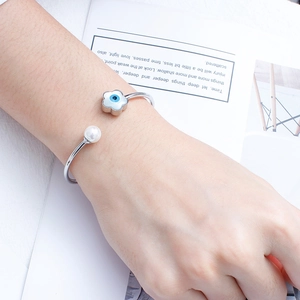 Detail of silver open bangle featuring evil eye flower charm and elegant white pearl