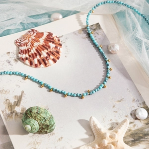 Detail of turquoise necklace with gold beads on ocean-themed background with shells