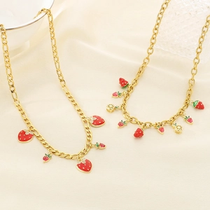 Gold strawberry pendant necklace with red enamel and green crystals on satin background