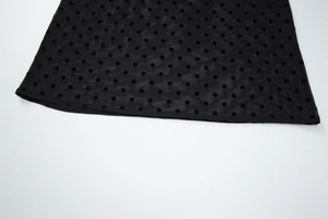 Détail du tissu en maille noire à pois avec des coutures précises sur l'ourlet de la robe