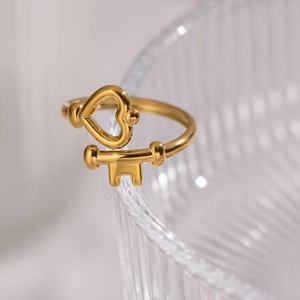 Close-up of golden key and heart open ring hanging on a textured glass edge