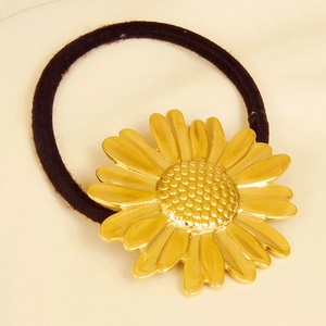 Detailed view of the gold daisy charm on a black elastic hair tie against beige fabric