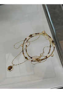 Detail of layered gold beaded necklace featuring an oval tiger eye stone pendant detail