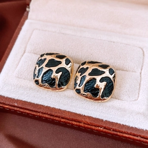 Close-up of golden square earrings with black leopard print enamel inlay in jewelry box