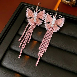 Dettaglio di orecchini a farfalla in zircone rosa con lunghe nappe su pelle nera