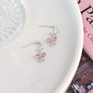 Details von rosa Kristall-Schmetterlingsohrringen mit kleinen Perlen auf weißem Teller