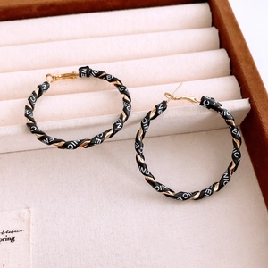 Detailed close-up of golden hoop earrings featuring black leather wrap and NICE text pattern