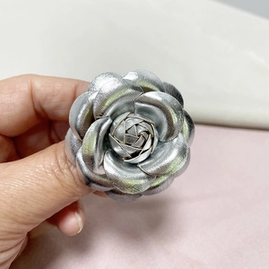 Detail of silver faux leather camellia flower brooch with metallic luster and layered petals