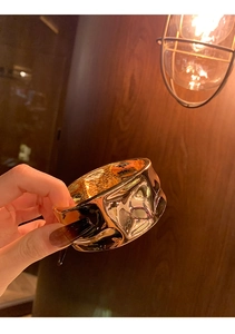 Nahaufnahme des goldenen breiten Armreifs mit unregelmäßiger Flüssigmetall-Struktur