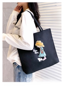 Detail of a large black canvas tote bag featuring a minimalist cartoon girl graphic print