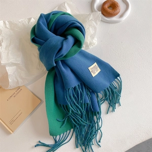 Detail of soft knit scarf in blue and green color block with tassel fringes and label