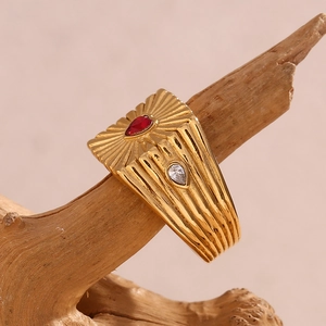 Detail of 18K gold ring with red teardrop stone displayed on a natural wood branch