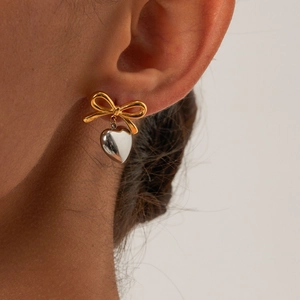 Close-up of dual-tone bow earrings with silver heart pendant worn by a model