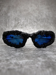 Detail of avant-garde sunglasses featuring textured black frames and vibrant blue lenses