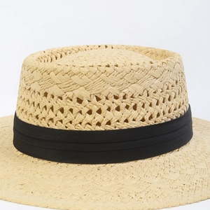 Detail of hand-woven straw boater hat with hollow-out pattern and black ribbon band