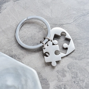 Polished stainless steel heart and puzzle keychain set on a gray marble background