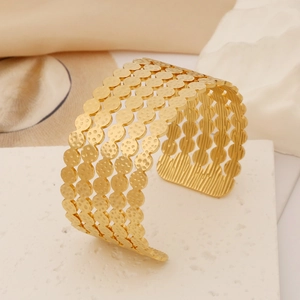 Detail of a wide gold stainless steel cuff featuring layered hollow hammered textures