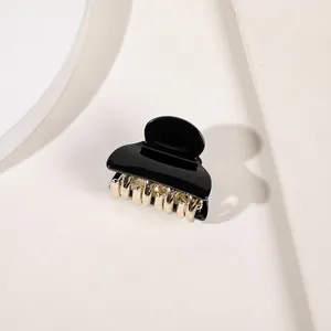 Detailed close-up of a small black glossy acrylic hair claw clip with golden metal teeth