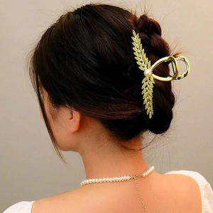 Elegant gold metal flower hair claw clip with rhinestones and pearl on dark hair
