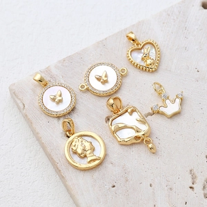 Macro shot of 14k gold-plated charms with natural mother-of-pearl on a beige stone slab