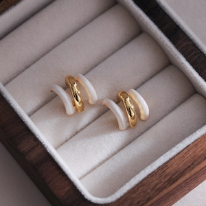Detailed view of C-shaped gold and white layered earrings on a soft velvet jewelry box