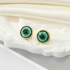 Detailed close-up of green resin evil eye stud earrings with sparkling gold metal edges