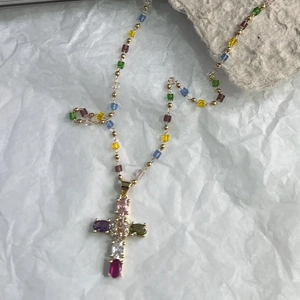 Détail d'un pendentif croix coloré avec pierres précieuses sur une fine chaîne dorée