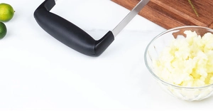 Détail du presse-purée en acier inoxydable avec poignée noire sur marbre blanc