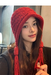 Close-up of chunky red knit beanie featuring long braided tassels for autumn winter