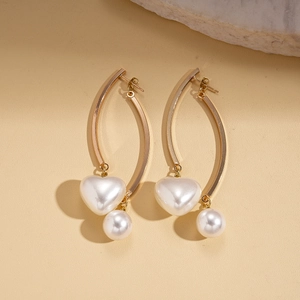Détail de boucles d'oreilles dorées avec pendentifs cœur et perle ronde sur pierre