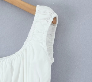 Detail shot of white sleeveless dress with elastic shoulder straps and ruched fabric texture