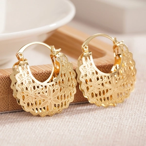 Macro shot of gold hollow flower earrings with intricate filigree on a wooden holder