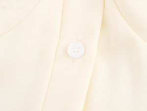 Macro shot of a classic white four-hole button on beige linen textured dress fabric