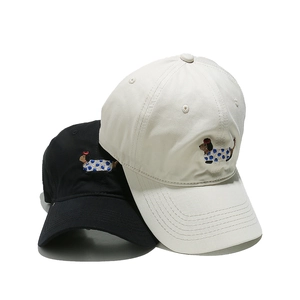 Detailed view of dog embroidery on cotton twill baseball caps in black and cream beige