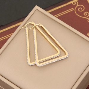 Dettaglio di orecchini a triangolo dorati con gemme su sfondo di libro d'epoca