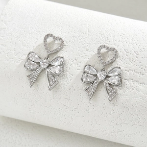 Detailed view of silver bow earrings with sparkling heart-shaped zircon inlay stones