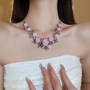 Detail of pink camellia necklace with green leaves, pearls, and rhinestones on a gold chain