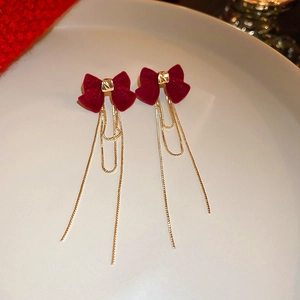 Macro view of velvet red bow earrings with long golden chain tassels on ceramic plate