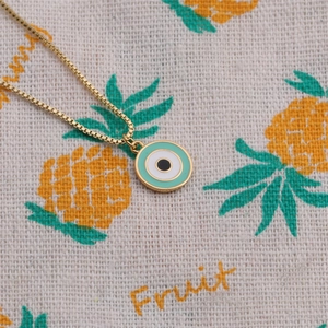 Golden necklace with mint green enamel evil eye pendant on pineapple pattern fabric
