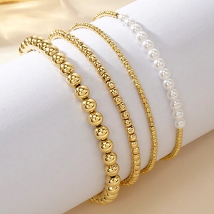 Set of 4 gold beaded bracelets with white pearls displayed on a white round stand