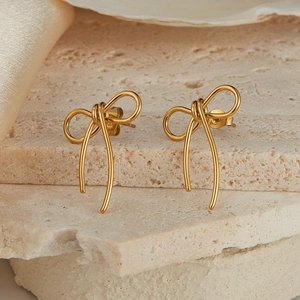 Detailed view of gold bow-shaped stainless steel stud earring on limestone and shell